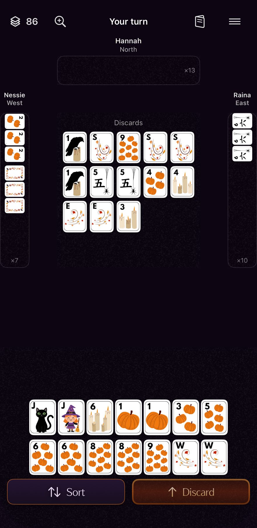 A mid-hand table on the app's Harvest tile set, midnight purple. It is your turn: thirteen tiles sit on the discard floor, West and East have each exposed tiles, and your own hand of pumpkins, candles, winds and two jokers, a black cat and a little witch, is racked below with Sort and Discard buttons